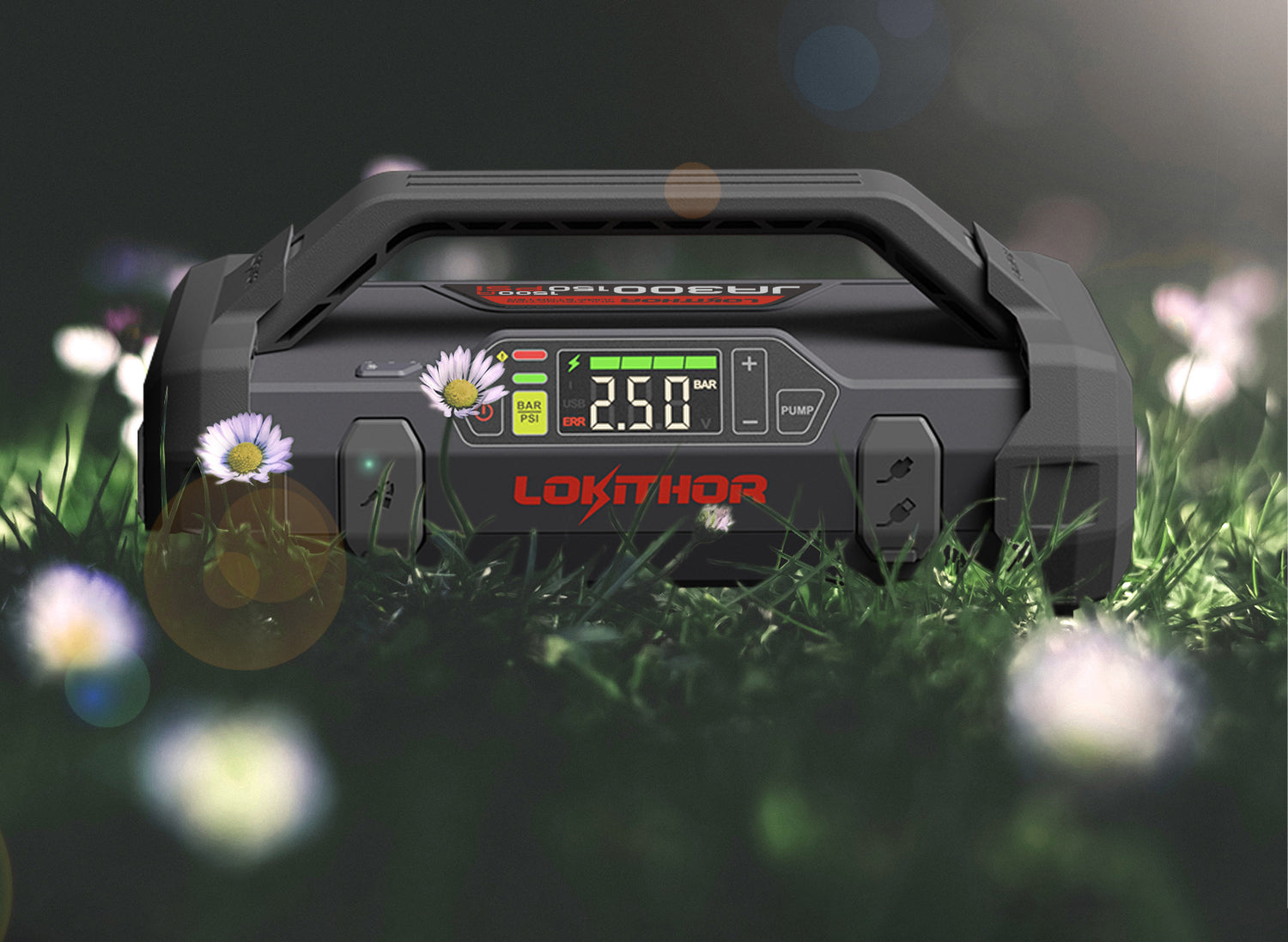 Portable jump starter on grass with digital display and daisies.