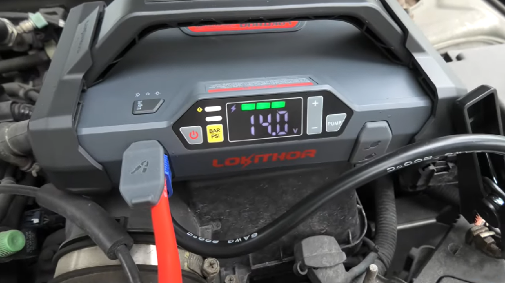 Jump starter displaying voltage in a car engine bay.